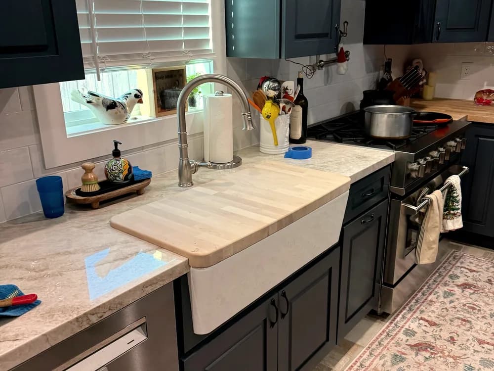 A kitchen with a farmhouse sink, marble counters and a bridge faucet