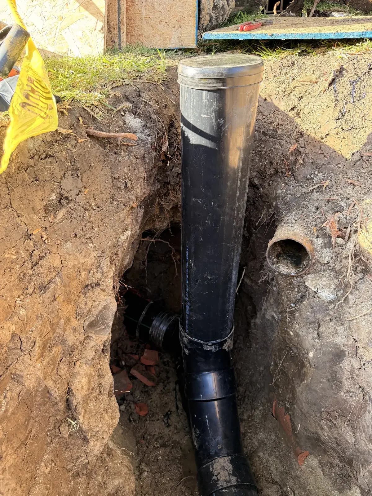 An excavation showing new sewer pipe standing beside the cut end of the old line