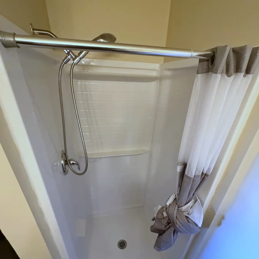 A step-in shower with a handheld on a slide bar and a built-in shelf, where a tub used to be