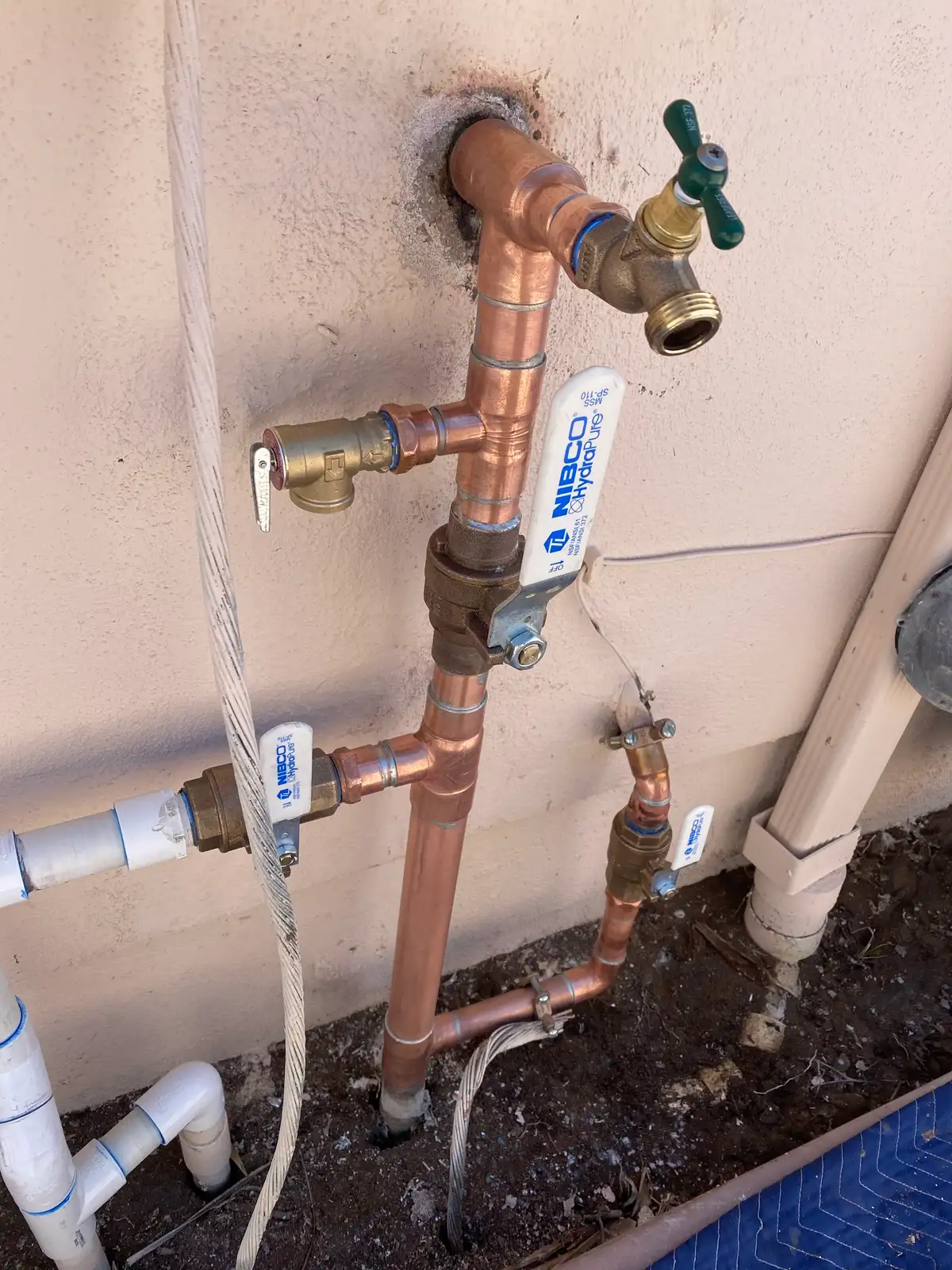 A copper manifold on an exterior wall with a hose bib and two shut-off valves